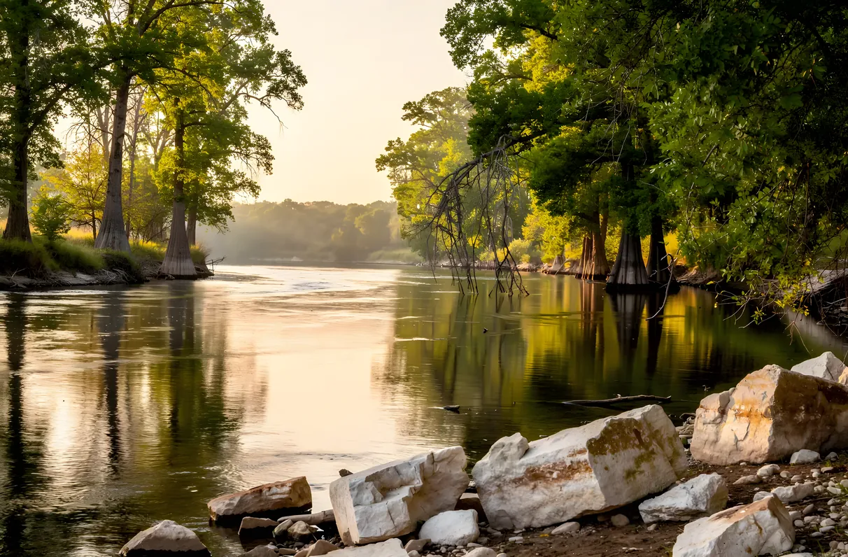 A calm bend of a Texas river lined with pecan and cypress trees and limestone rocks along the bank